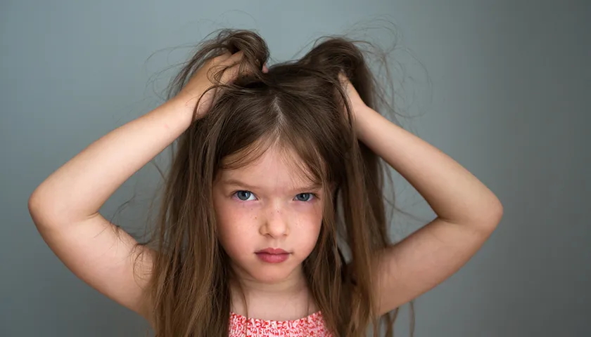 El principal síntoma de los piojos en niños es el picor intenso en la cabeza. niña con pelo largo rascándose el cuero cabelludo